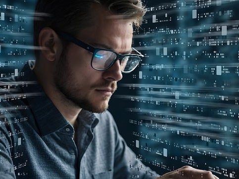Verarbeitungstätigkeiten Mann mit Brille, fokussiert auf einen Computer, umgeben von binären Daten.