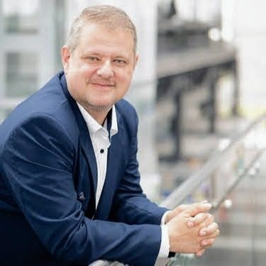 Auf dem Bild ist der CEO-Falk Boede von DataSafeguard Consulting EU zu sehen Mann in Anzug lehnt an Geländer und lächelt in eine moderne Umgebung.