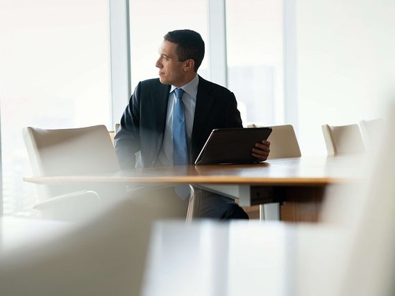 Datenschutzfolgeabschätzung, bild zum Text Mann mit Tablet sitzt nachdenklich an einem Konferenztisch in einem modernen Büro.